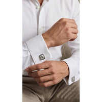 Close-up of a person adjusting the cuff of a white shirt with cufflinks.
