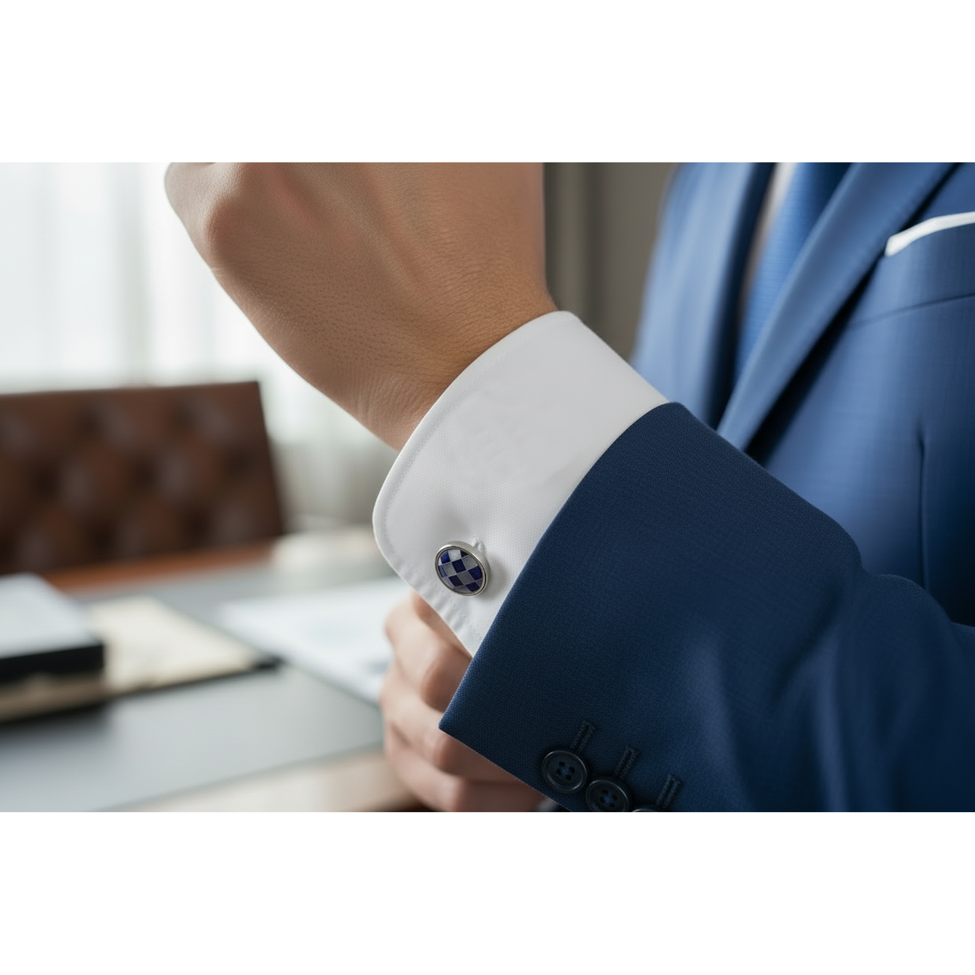 Close-up of a person adjusting their blue suit cuff with a decorative button, blurred office background.