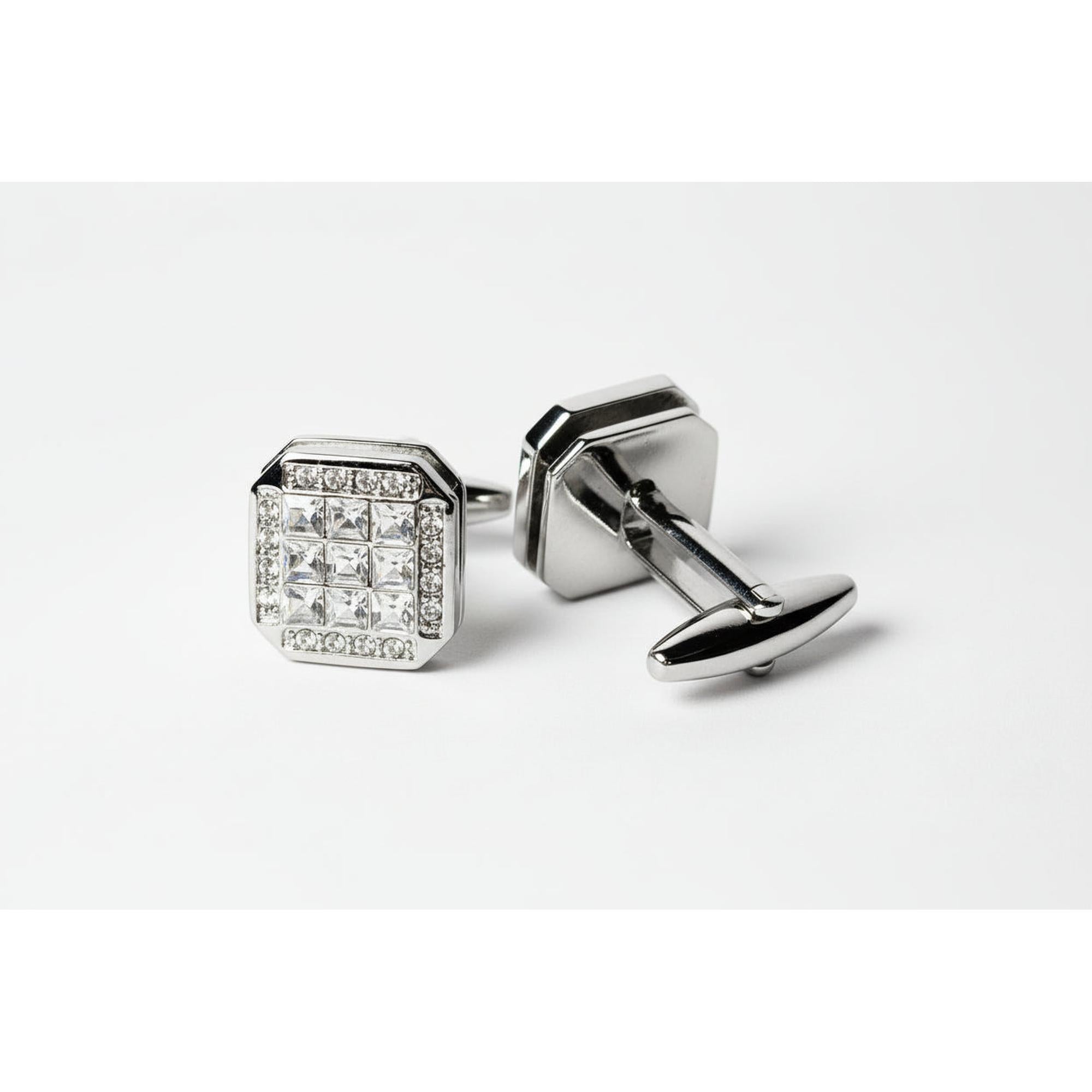 Pair of silver cufflinks with one featuring clear gemstones on a light gray background