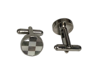 A pair of silver-toned metal cufflinks on a Plan background. One cufflink is shown from the front, featuring a round face with a black and white checkered pattern, and the other is shown from the side/back, displaying its polished silver-toned metal construction.