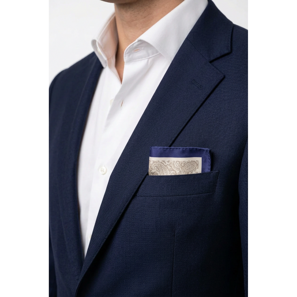 A close-up of a man wearing a navy blue suit jacket over a white dress shirt, with a patterned navy and beige pocket square tucked into the breast pocket.