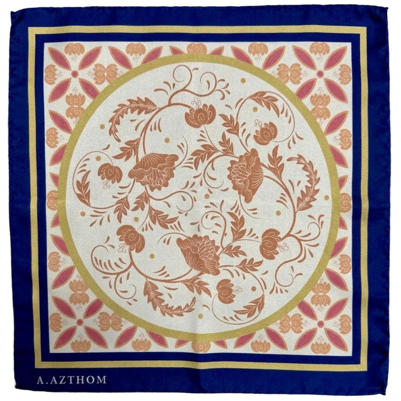 A square silk scarf with a traditional floral pattern, featuring a navy blue border, a gold inner border, and a central cream circle with terracotta-colored botanical motifs. The brand name 'A.