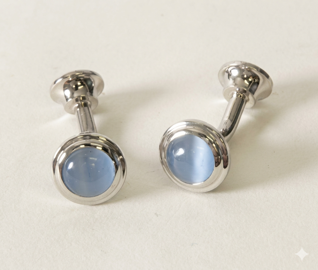 A pair of silver-toned cufflinks with oval light blue cateye, displayed on a clean off-white background.